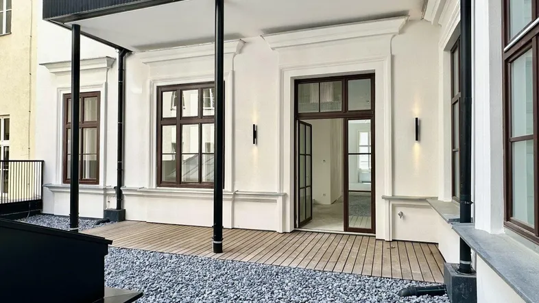 Geräumige Terrasse mit Holzboden und Kiesbereich, direkt vom Innenraum zugänglich, ideal für Entspannung im Freien.