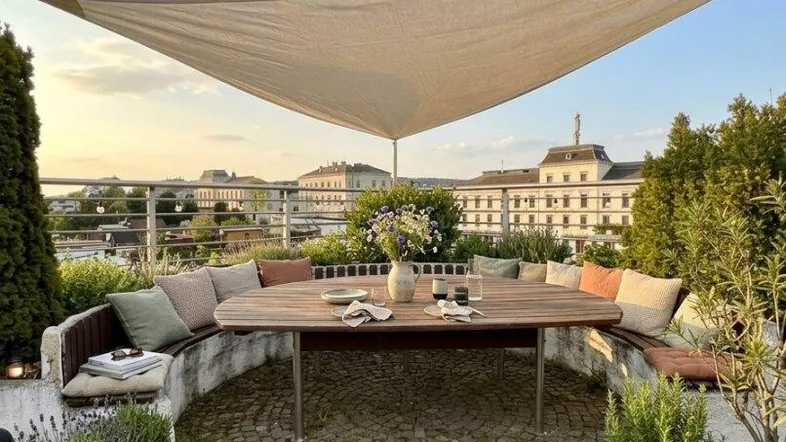 Gemütliche Dachterrasse mit Sitzbereich, Sonnensegel und Blick auf die Stadt.