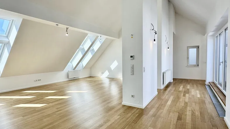 Helles, offenes Wohnzimmer mit Dachschrägen, Parkettboden und großen Dachfenstern.
