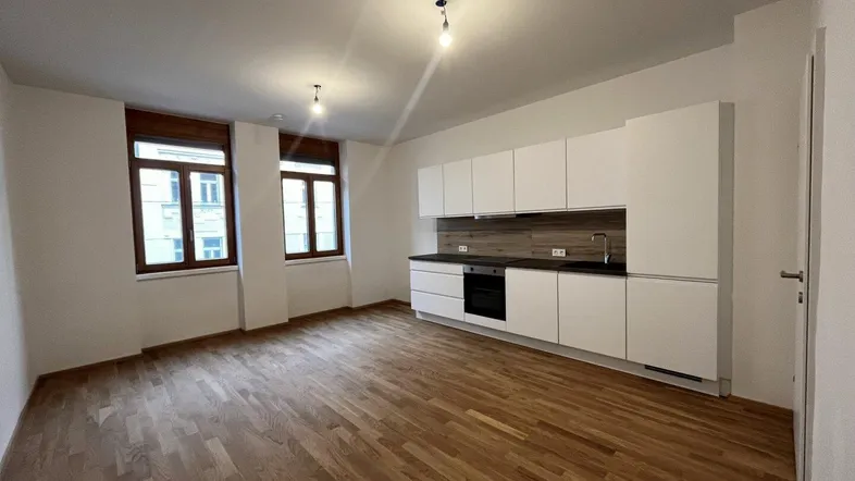Heller Wohnbereich mit integrierter weißer Küche, Holzboden und zwei Fenstern.