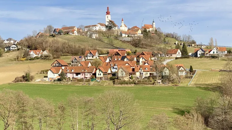 Panoramablick auf ein malerisches Dorf auf einem Hügel mit Kirche und umliegender Landschaft.