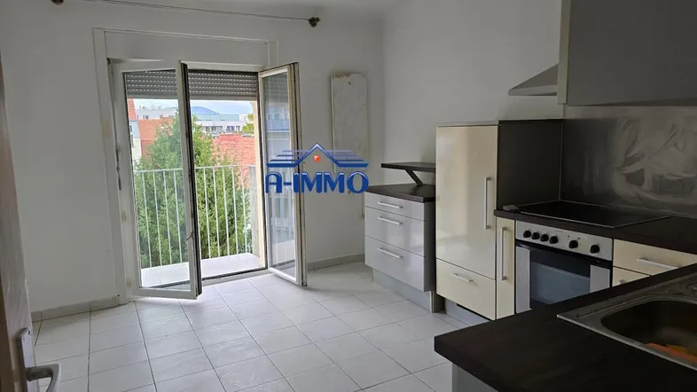 Helle Küche mit Fliesenboden, einfachen Einbauschränken und direktem Zugang zum Balkon mit Blick ins Grüne.