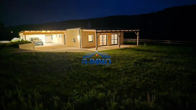 Modernes Einfamilienhaus bei Nacht mit beleuchtetem Carport und weitläufigem Grundstück.