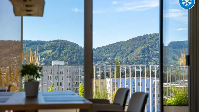 Heller Innenraum mit Panoramablick auf grüne Hügel und die Stadt.