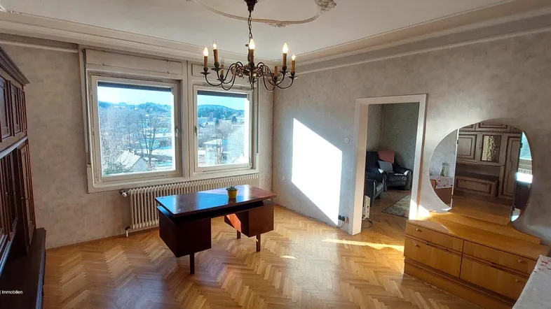 Klassisch eingerichtetes Zimmer mit Parkettboden, Stuckdecke und Blick auf die Umgebung.