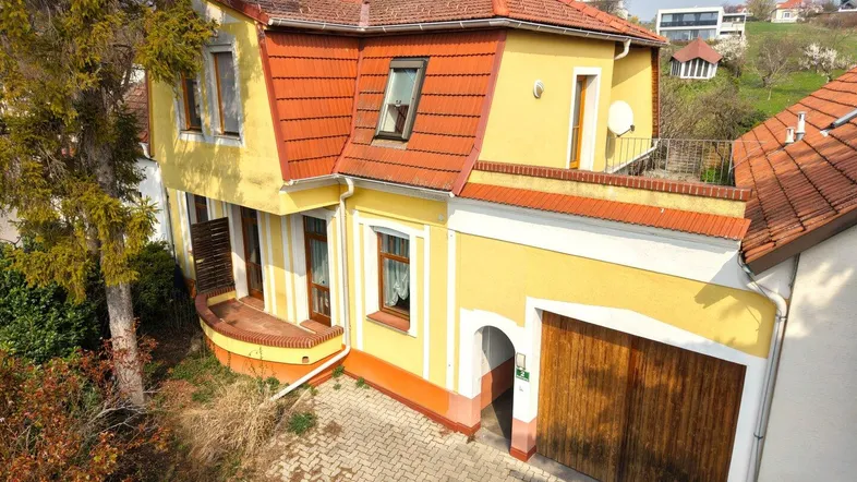 Gelbes Haus mit rotem Ziegeldach, Garage und gepflasterter Einfahrt in ländlicher Umgebung.