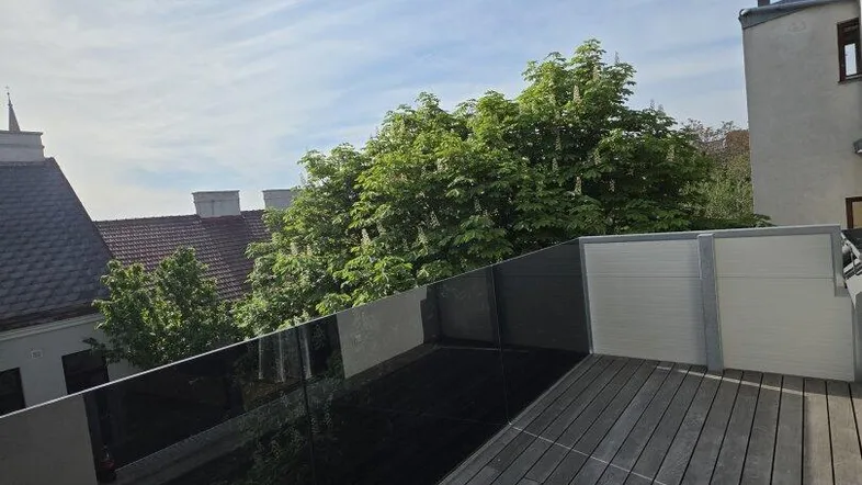 Sonnige Dachterrasse mit Holzboden und Glasgeländer, bietet einen weiten Blick über die Dächer.