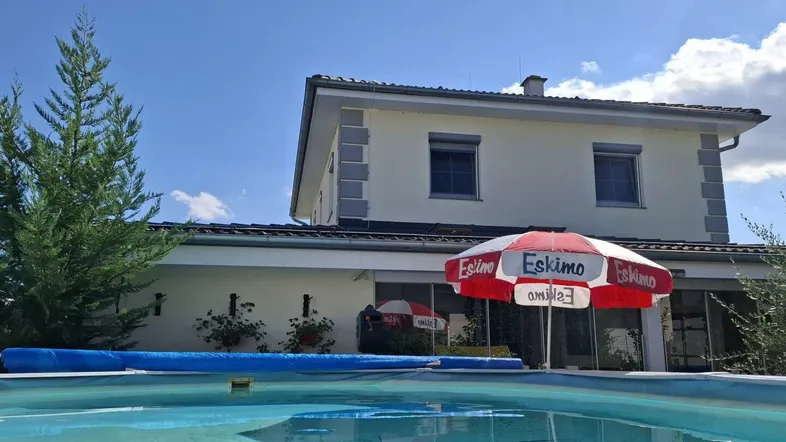 Außenansicht des Hauses mit privatem Swimmingpool und Sonnenschirm im Gartenbereich.