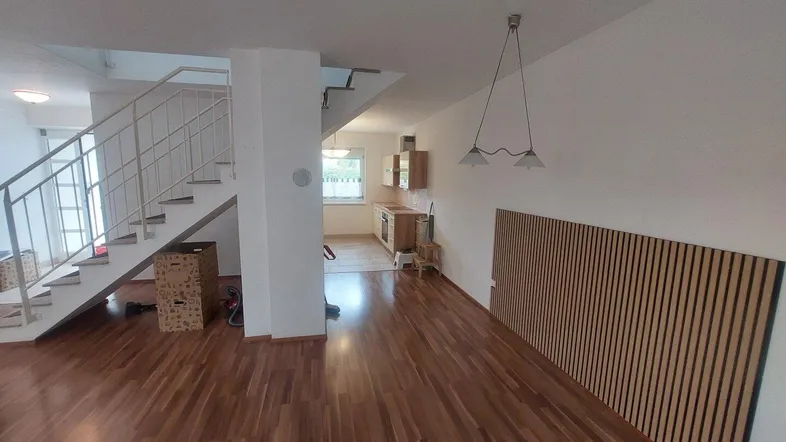 Geräumiger Wohnbereich mit Holzfußboden, offener Treppe und Blick in die Küche.