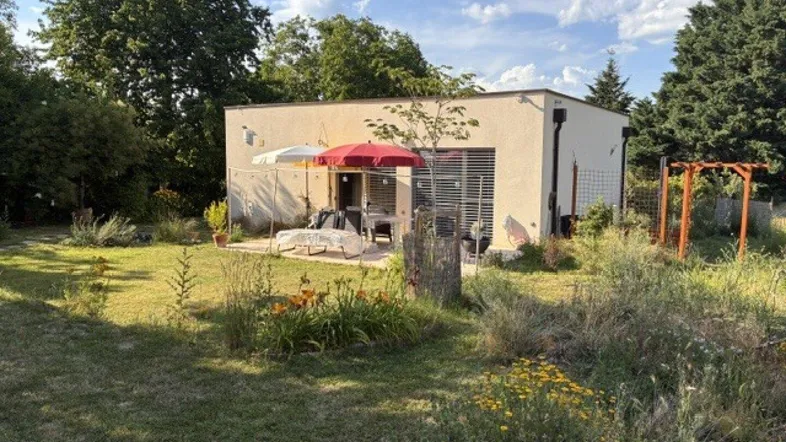 Modernes Haus mit sonniger Terrasse und großem Garten unter blauem Himmel.