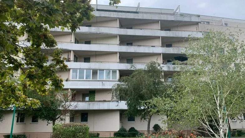 Mehrstöckiges Wohngebäude mit zahlreichen gestaffelten Balkonen und einer gepflegten Grünanlage im Vordergrund.