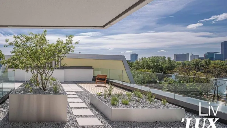 Moderne Dachterrasse mit Pflanzenbeeten, Kies und Stadtblick unter blauem Himmel.