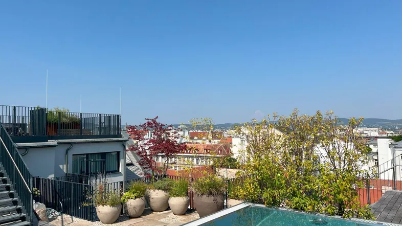 Dachterrasse mit Infinity-Pool und weitem Blick über die Stadt an einem sonnigen Tag.