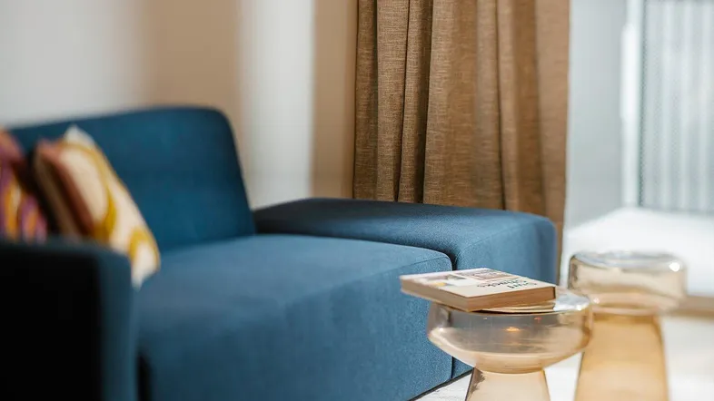 Gemütliches Wohnzimmer mit blauem Sofa, modernen Beistelltischen und Zugang zum Balkon.
