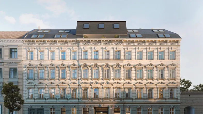 Historische Fassade eines Mehrfamilienhauses mit aufwendigen Verzierungen und modernem Dachausbau.
