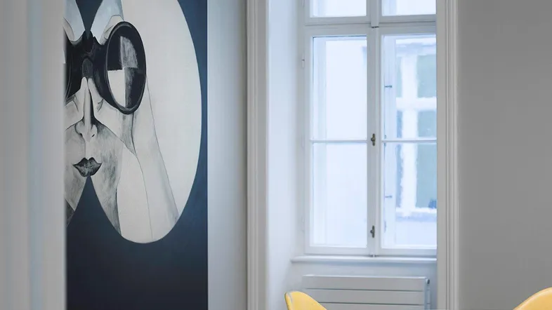 Heller Innenraum mit modernem Kunstwerk, gelben Stühlen und großem Fenster, das viel Tageslicht hereinlässt.
