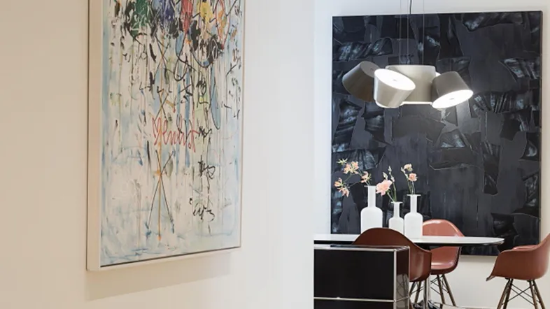 Ein stilvoller Essbereich mit modernem Design, einem großen Kunstwerk und einer auffälligen Deckenleuchte.