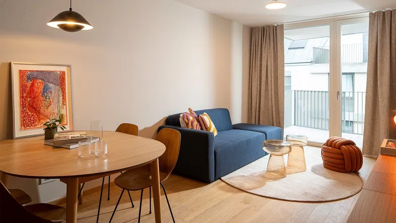 Helles Wohn- und Esszimmer mit modernem Sofa, Holztisch und Zugang zum Balkon.