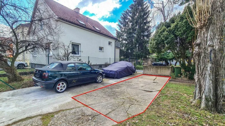 Außenansicht eines Wohnhauses mit Einfahrt und einem markierten Parkplatzbereich im Garten.