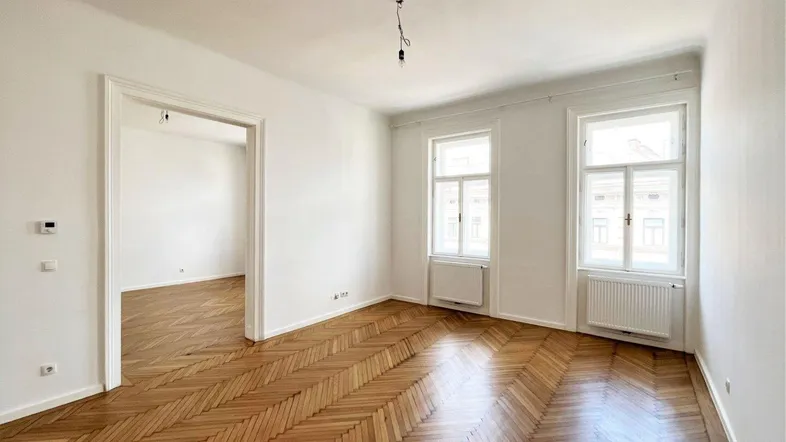 Helles, leeres Wohnzimmer mit Fischgrätparkett und hohen Fenstern, bereit zum Einzug.