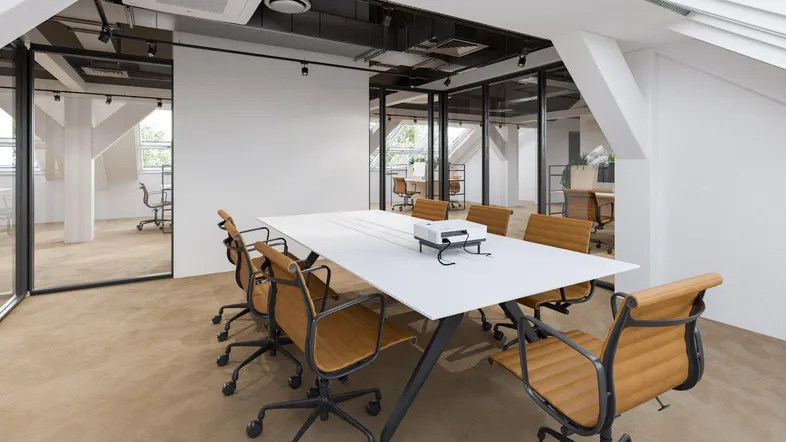 Moderner Konferenzraum in einem Dachgeschossbüro mit schrägen Wänden, großen Fenstern und einem Projektor auf dem Tisch.