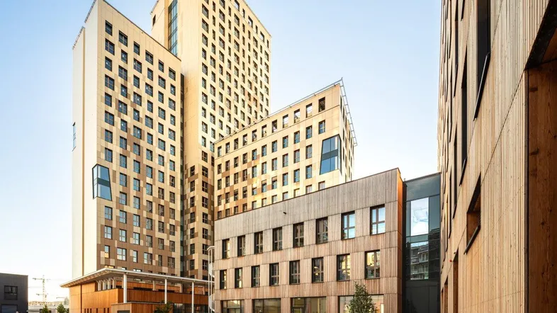 Moderne Hochhäuser mit Holzfassaden und gepflegter Außenanlage unter blauem Himmel, die eine zeitgenössische Architektur zeigen.