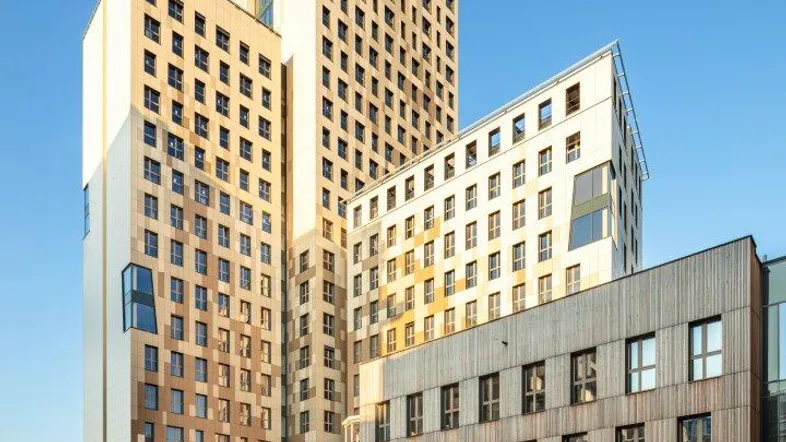 Moderne Hochhäuser mit Holzfassaden und gepflegter Außenanlage unter blauem Himmel.
