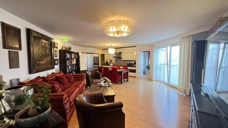 Geräumiger offener Wohn- und Essbereich mit Holzboden, rotem Sofa und Zugang zum Balkon.