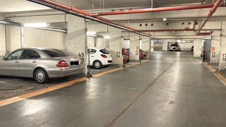 Geräumige Tiefgarage mit mehreren Parkplätzen, sichtbaren Rohren an der Decke und Beleuchtung.