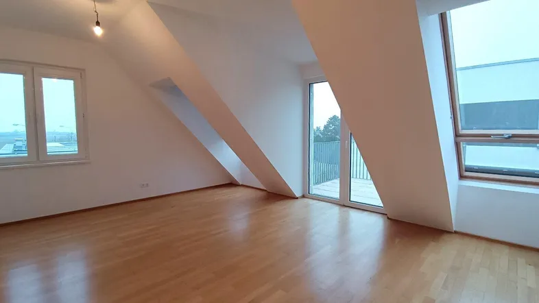 Helles Zimmer mit Dachschrägen, Parkettboden und Zugang zu einem Balkon.