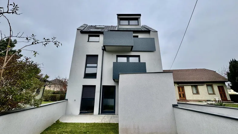 Modernes Mehrfamilienhaus mit weißer Fassade, grauen Balkonen und kleinem Vorgarten.