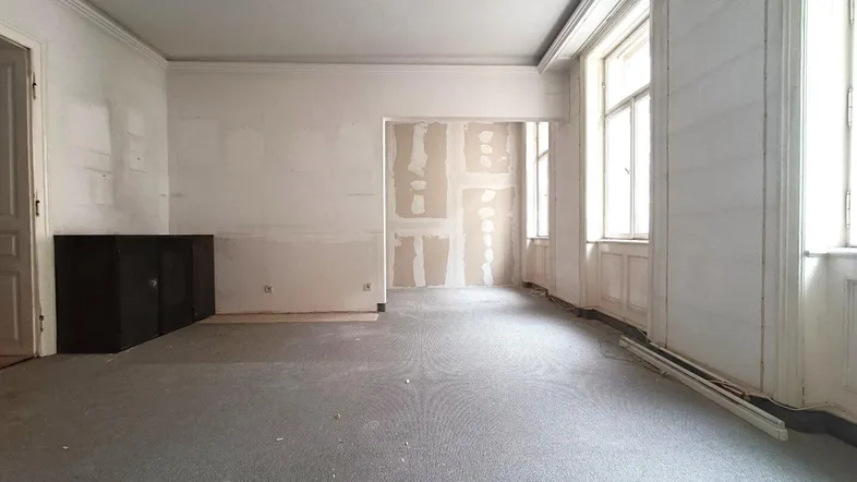 Geräumiger Wohnraum mit Teppichboden und großen Fenstern, bereit für die Renovierung.