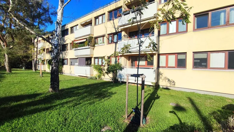 Gelbes Mehrfamilienhaus mit Balkonen und grüner Rasenfläche im Vordergrund unter blauem Himmel.