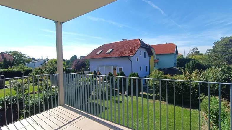 Geräumiger Balkon mit Fliesenboden und Blick auf den grünen Garten und Nachbarhäuser.