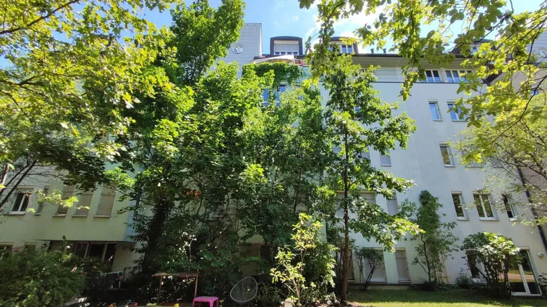 Grüne Fassade eines Mehrfamilienhauses mit Bäumen und einem kleinen Spielbereich im Vordergrund.