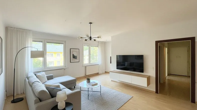 Helles Wohnzimmer mit modernem Sofa, Holzboden und Blick ins Grüne durch große Fenster.