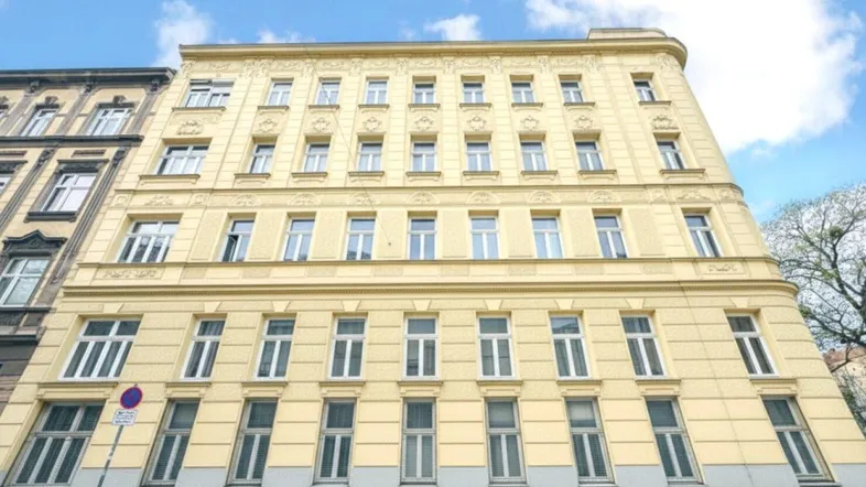 Historisches Mehrfamilienhaus mit klassischer Fassade und vielen Fenstern unter blauem Himmel.