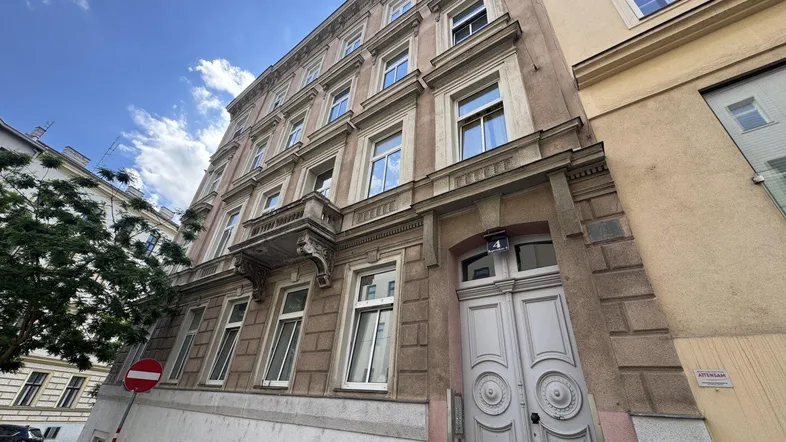 Historische Fassade eines Altbaus mit mehreren Stockwerken und klassischen Fenstern unter blauem Himmel.