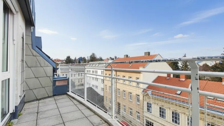 Geräumiger Balkon mit Fliesenboden und Metallgeländer, bietet einen weiten Blick über die Dächer der Stadt.