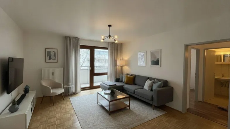 Helles Wohnzimmer mit modernem Sofa, Parkettboden und Zugang zum Balkon.