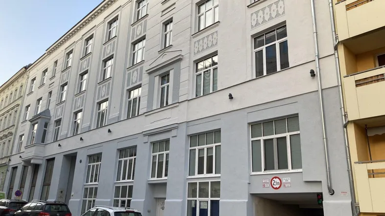Fassade eines gut erhaltenen Mehrfamilienhauses mit großen Fenstern und Einfahrt zur Tiefgarage.
