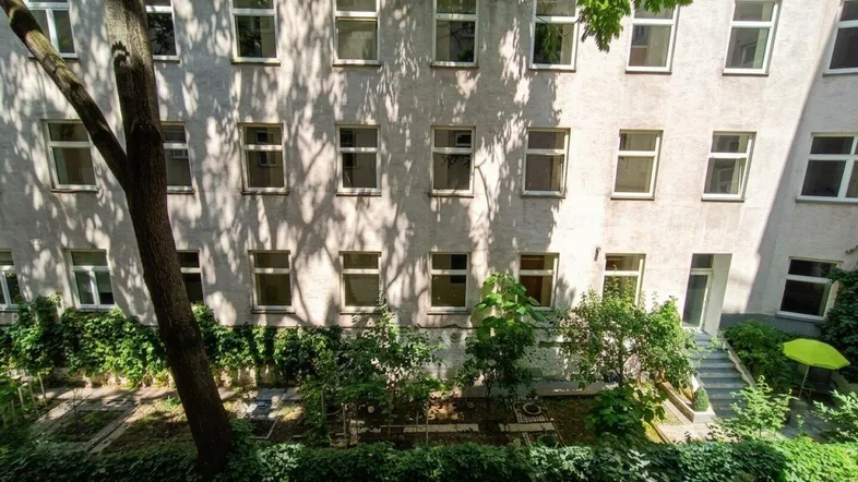 Blick in einen grünen Innenhof mit üppiger Bepflanzung und der Rückseite eines Wohngebäudes.