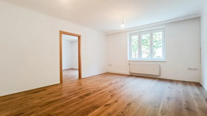 Helles, leeres Zimmer mit neuem Holzboden und weiß gestrichenen Wänden, bereit zur Einrichtung.