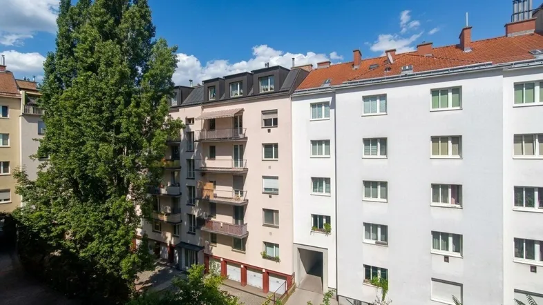 Mehrere Wohngebäude mit Balkonen und Bäumen unter blauem Himmel in einer städtischen Umgebung.