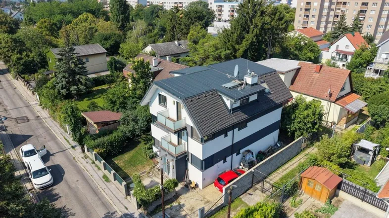 Luftaufnahme des modernen Hauses mit dunklem Dach und weißer Fassade in grüner Umgebung.