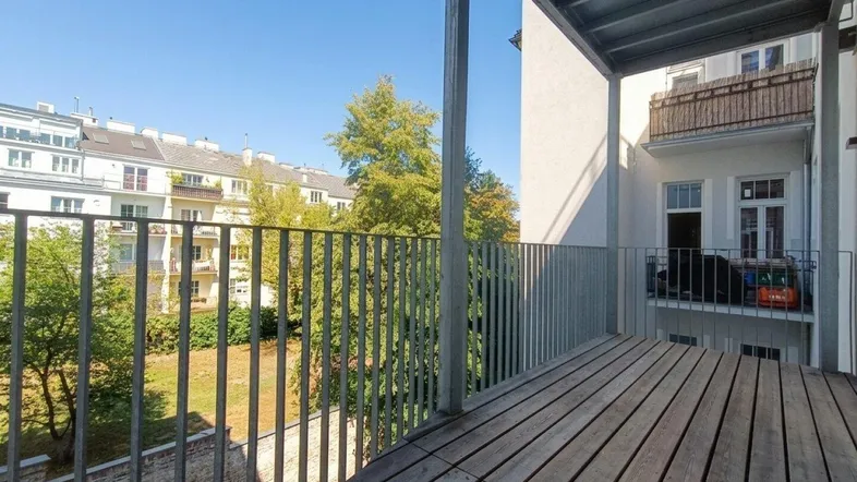 Geräumiger Balkon mit Holzdielen und Blick auf den grünen Innenhof und umliegende Gebäude.