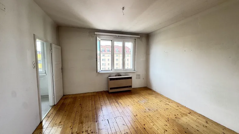 Heller Raum mit Holzdielenboden, weißen Wänden und Blick auf die Stadt durch das Fenster.