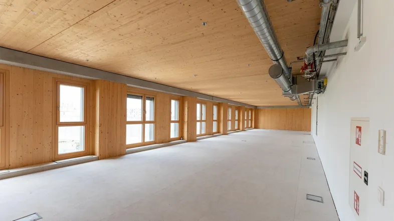 Großer, leerer Büroraum mit Holzwänden und -decke, vielen Fenstern und sichtbaren Lüftungsrohren.