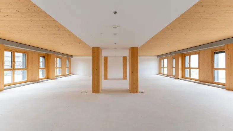 Großer, heller Gewerberaum mit Holzsäulen und Holzdecke, umgeben von zahlreichen Fenstern.
