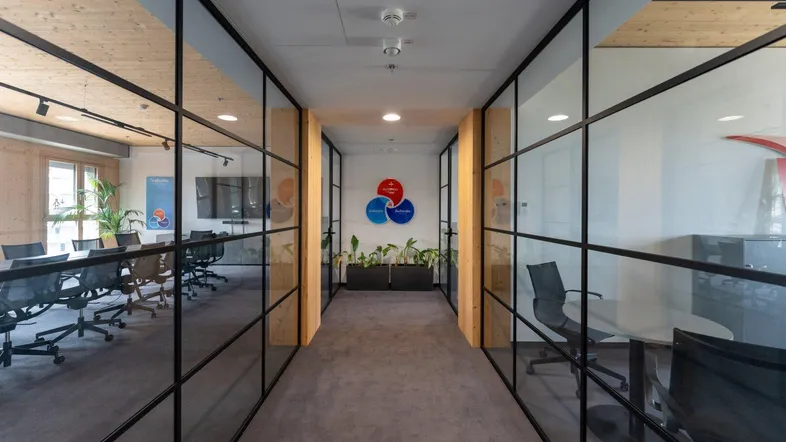Modernes Büro mit Glaswänden, Teppichboden und Holzakzenten, das eine helle und offene Arbeitsumgebung schafft.